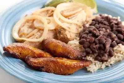 Closeup of Cuban dinner with focus on fried sweet plantains. Marinated roast pork with black beans and rice complete the meal.