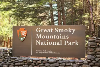Great Smoky Mountains National Park entrance sign with stone surrounding and trees and sunshine in the background